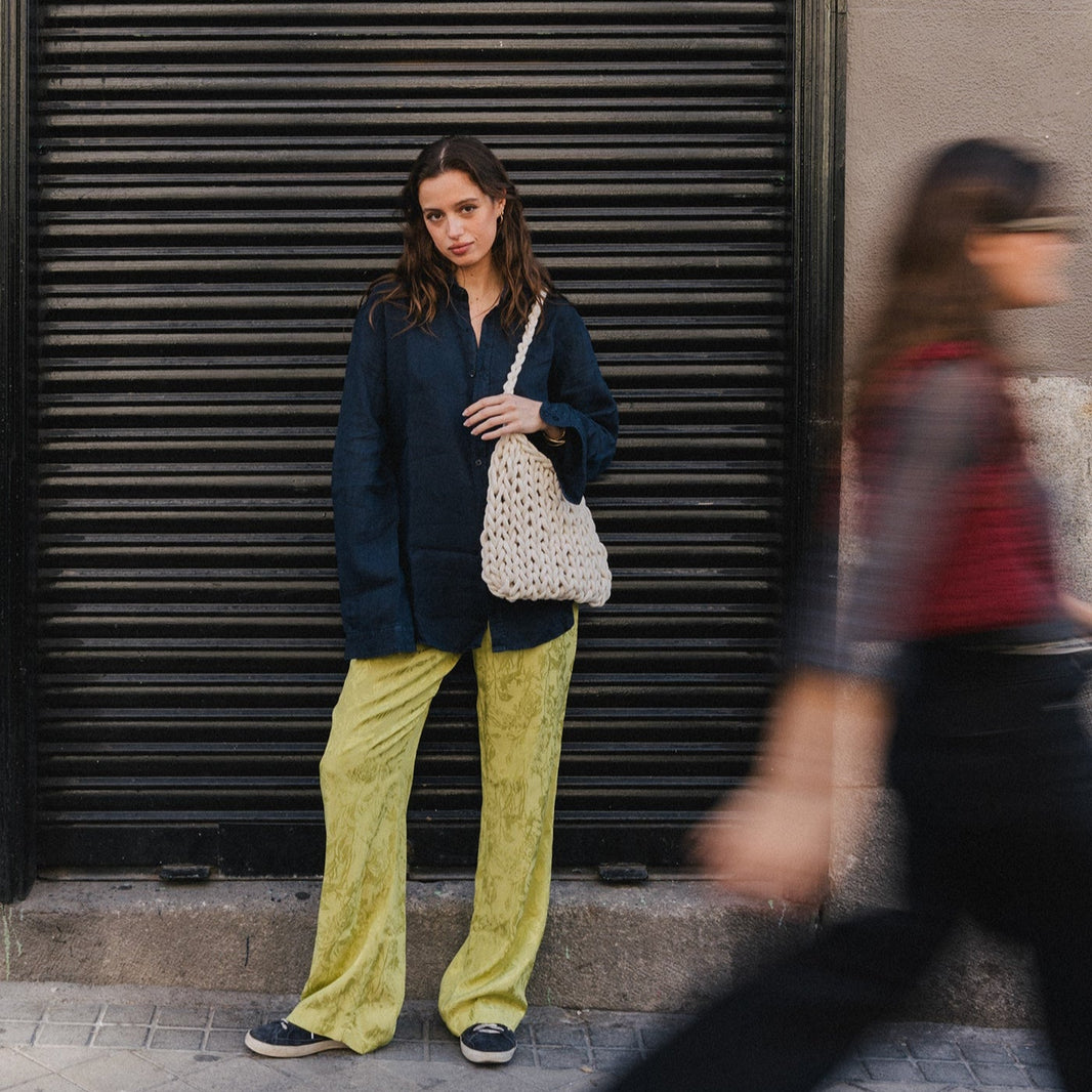 Woman in a blue blazer and yellow pants standing against a closed metal shutter.